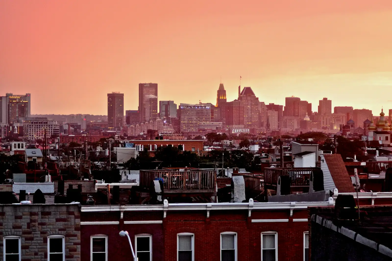 Baltimore rowhouse rooftops with the downtown skyline at sunset